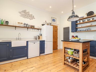 A kitchen with blue cabinets white appliances wooden floor and island at The Water House in Falmouth