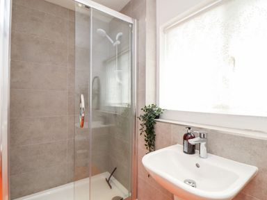 A bathroom with a glass shower enclosure a handheld showerhead a white sink with a faucet a soap dispenser and a small plant on the windowsill at The Water House in Falmouth