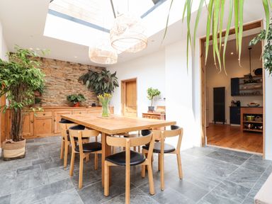 A dining area with a wooden table and six chairs next to a stone wall and wooden cabinets at The Water House in Falmouth