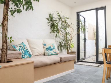 A seating area with beige cushions and blue patterned pillows next to large plants and glass doors at The Water House in Falmouth