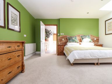 A bedroom with a bed with a wicker headboard two bedside tables wooden chest of drawers and green walls at The Water House in Falmouth