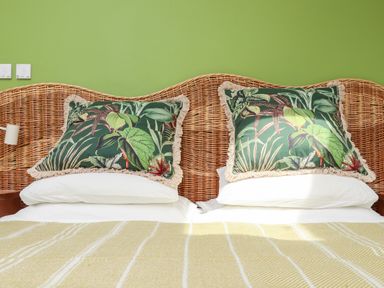 A bed with rattan headboard green leaf patterned pillows white sheets and a yellow striped blanket at The Water House in Falmouth
