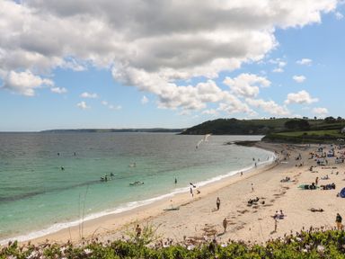A beach with people walking and swimming and green hills in the background at The Water House in Falmouth