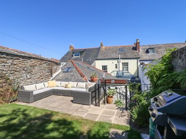 An outdoor patio with a sectional sofa and cushions a barbecue grill and potted plants at The Water House in Falmouth
