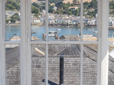 A window view showing rooftops with chimneys and boats on water with houses on the opposite shore at The Water House in Falmouth