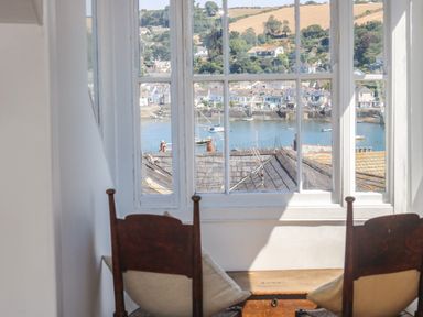 A window with a view of rooftops water and houses beyond with two wooden chairs in front at The Water House in Falmouth