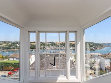 A window view overlooking rooftops, a river with boats, and green hills at The Water House in Falmouth