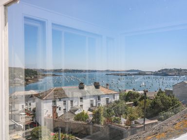 A view of a coastal town with white buildings and many boats on the water seen through a window at The Water House in Falmouth