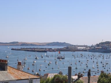 A harbor with many sailboats and ships in the water with industrial buildings and hills in the background at The Water House in Falmouth