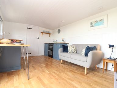 A kitchen and sitting area with a grey sofa and blue cabinets at Sebright in St Austell