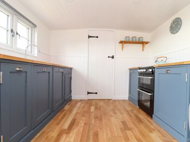 A kitchen with blue cabinets wooden countertops an oven a kettle a wall clock and a door at Sebright in St Austell
