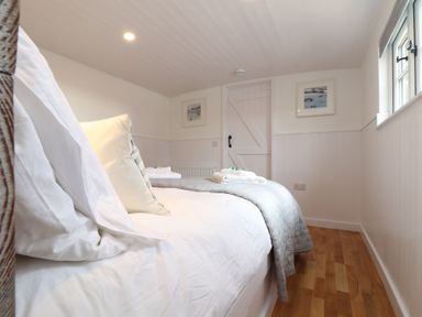 A bedroom with a bed pillows folded towels wooden floor white walls and a door at Sebright in St Austell