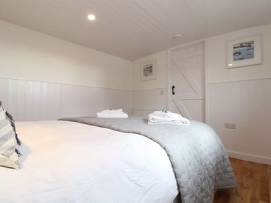 A bedroom with a bed covered with white and gray linens towels folded on the bed white paneled walls and wooden floor at Sebright in St Austell