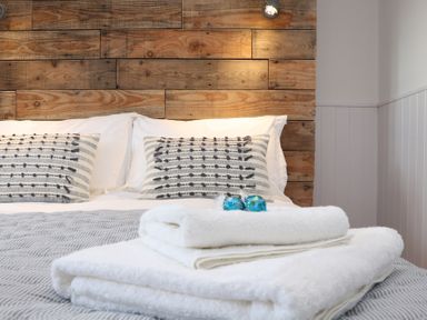 A bed with patterned pillows a wooden headboard and folded white towels at Sebright in St Austell