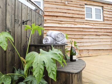 An outdoor wooden hot tub with towels and a bottle of champagne next to a wooden house at Sebright in St Austell