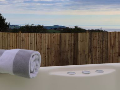 A rolled towel on the edge of a white hot tub with a wooden fence and distant hills and sea in the background at Sebright in St Austell
