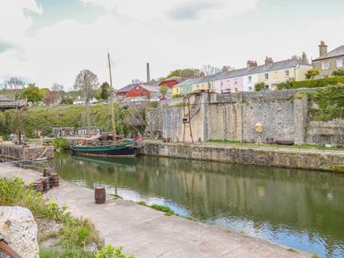 A dock with a moored sailboat stone walls and a row of houses in the background at Sebright in St Austell