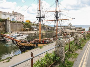A harbor with a docked tall ship and smaller boats next to houses and a stone wall at Sebright in St Austell