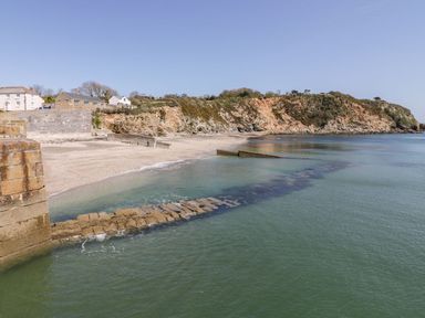 A beach with a stone sea wall and houses near cliffs by the ocean at Sebright in St Austell