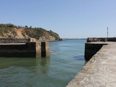A stone pier extending into the sea with people sitting on it and a hillside in the background at Sebright in St Austell