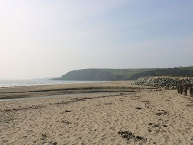 A sandy beach with a rocky breakwater and green hills in the background at Sebright in St Austell