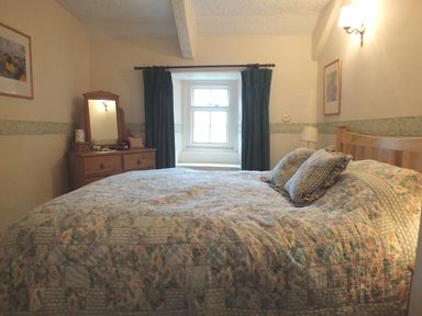 A bedroom with a large bed floral bedding curtains and a wooden dresser with a mirror at Milkwood Cottage Fishguard Pembrokeshire