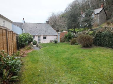 A backyard with a grass lawn and shrubs surrounded by wooden and stone fences with cottages in the background at Milkwood Cottage Fishguard Pembrokeshire