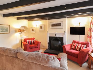 A living room with two red armchairs a beige sofa a fireplace and a wall mounted television at Milkwood Cottage in Fishguard Pembrokeshire