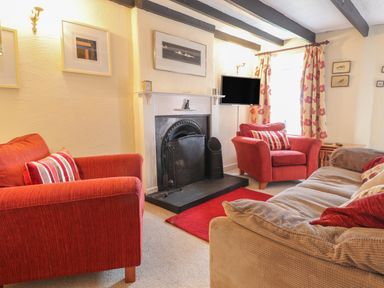 A living room with red armchairs a beige sofa a fireplace and a wall-mounted TV at Milkwood Cottage in Fishguard Pembrokeshire