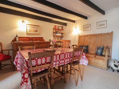 A dining room with a wooden table covered by a red and white tablecloth surrounded by wooden chairs and bench at Milkwood Cottage in Fishguard Pembrokeshire