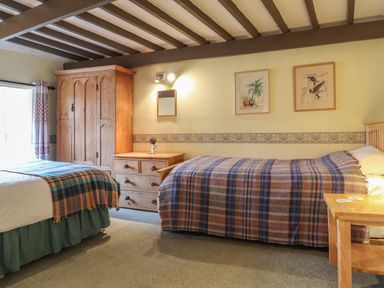 A bedroom with two beds a wooden wardrobe a wooden chest of drawers and framed pictures on the wall at Milkwood Cottage Fishguard Pembrokeshire