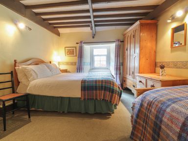 A bedroom with two beds a wardrobe dresser chair and window at Milkwood Cottage in Fishguard Pembrokeshire