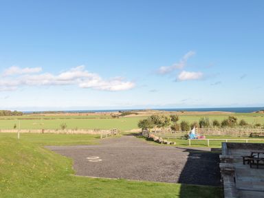 A countryside view with grassy fields and a gravel area near a patio at Stable D'or Embleton