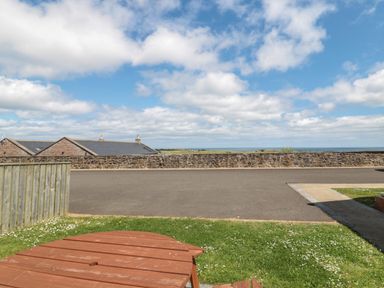 A grassy backyard with a wooden picnic table and a view of a stone wall and rooftops under a partly cloudy sky at Stable D'or in Embleton