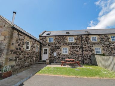 A stone cottage with a picnic table on a patio and grass area outside at Stable D'or in Embleton