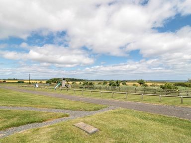 A grassy outdoor area with a children's playground and wooden fence under a cloudy sky at Stable D'or in Embleton