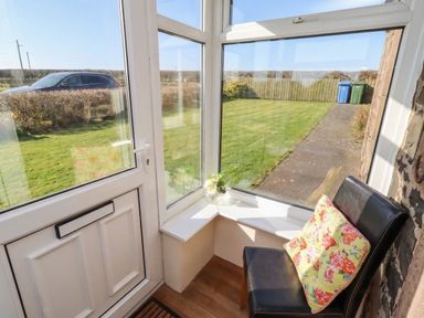 A conservatory with a chair and views of the lawn at The Retreat in Embleton