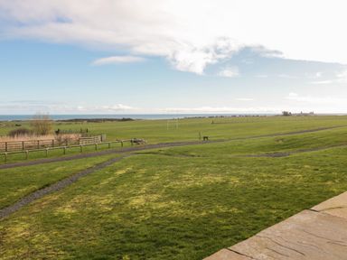 An open grassy field with a gravel path and a wooden fence near the coast at Low Croft in Embleton