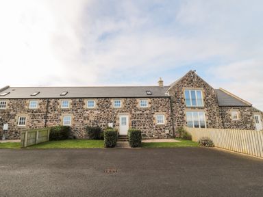 A stone building with multiple windows and doors and a paved area in front at Low Croft in Embleton