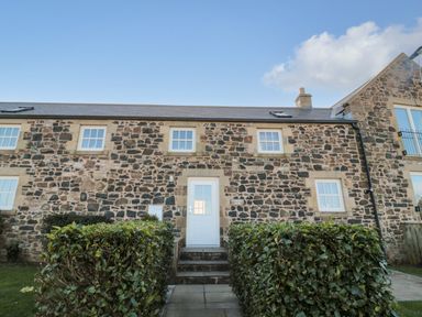 Front entrance of a stone cottage with a white door and windows surrounded by hedges at Low Croft in Embleton