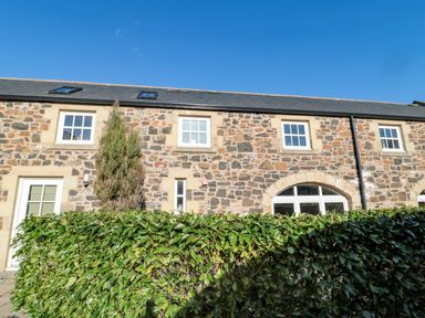 A stone building with four windows a door and a hedge in front at Low Croft in Embleton