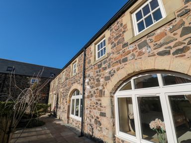 Stone exterior of a building with arched windows and a patio at Low Croft in Embleton
