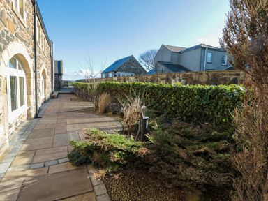 A stone house with a tiled pathway and hedges in the garden at Low Croft in Embleton