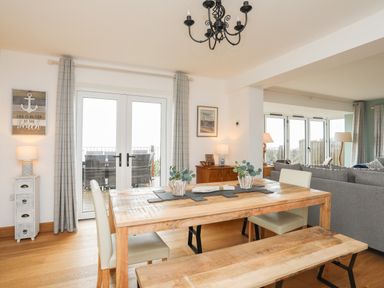 A dining area with wooden table and bench chairs next to a living room with gray sofas at Red Ridge in Llandanwg near Harlech