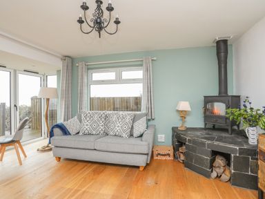 A living room with a gray sofa and patterned cushions next to a black wood stove and a window at Red Ridge in Llandanwg near Harlech