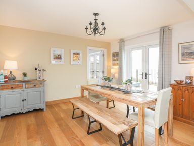 A dining room with a wooden table and bench and two chairs near glass double doors at Red Ridge in Llandanwg near Harlech