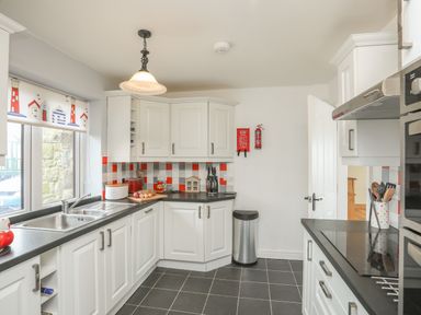 A kitchen with white cabinets black countertops and tiled floor at Red Ridge in Llandanwg near Harlech