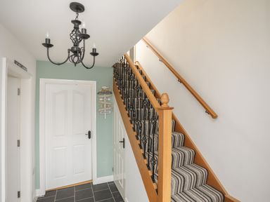A hallway with a staircase with striped carpet and decorative railing at Red Ridge in Llandanwg near Harlech