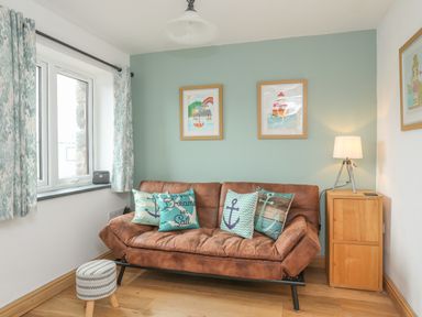 A room with a brown sofa with decorative cushions next to a window and a wooden side table with a lamp at Red Ridge in Llandanwg near Harlech