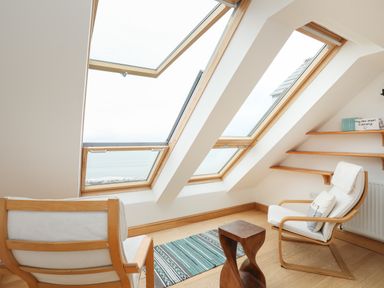 An attic room with two wooden chairs with cushions a small wooden side table a striped rug and three skylight windows at Red Ridge in Llandanwg near Harlech
